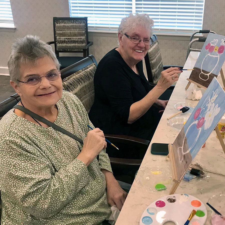 Two women, senior residents with paint brushes in hand, passionately create a masterpiece on canvas - a beautiful vase of flowers. Art knows no age limits!