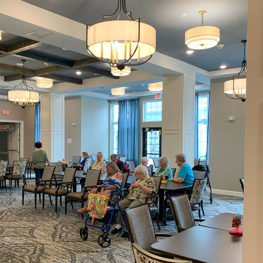 Dining area at the Boulevard of Saint Peters Senior Living, featuring residents seated at tables, large windows, elegant lighting fixtures, and a patterned carpet.